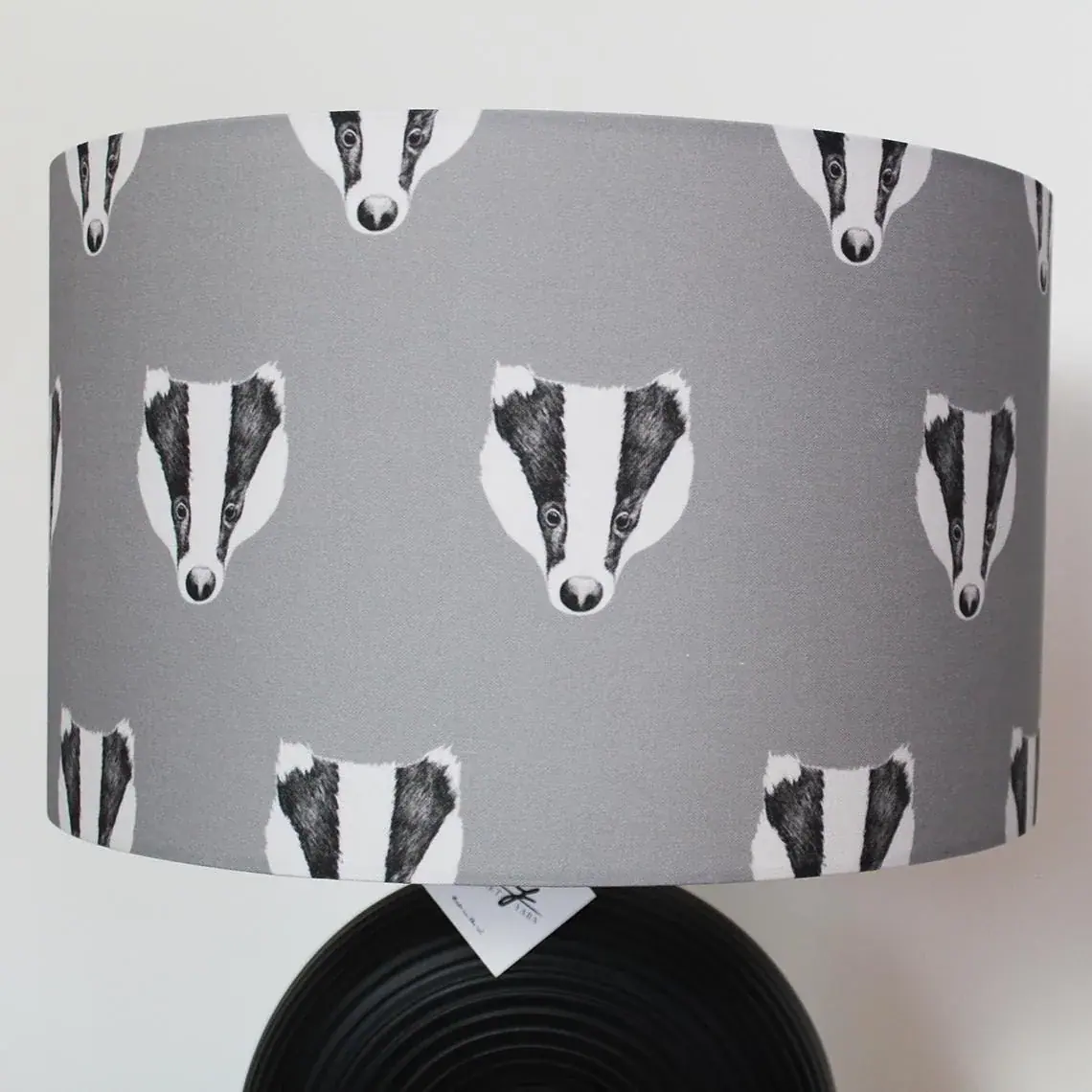 Badger lampshade: a grey drum shade covered in rows of hand-drawn black and white badger faces