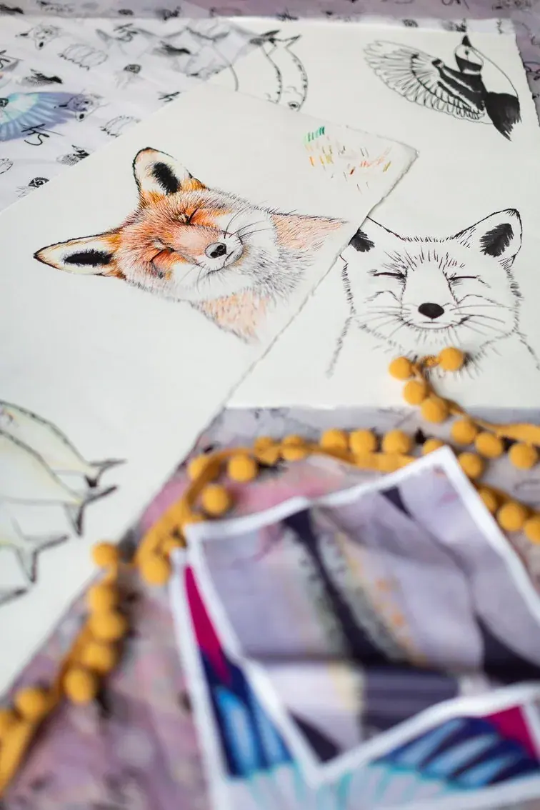 Rachael's fox sketches and printed drawings spread across her desk with a mustard pom-pom trim